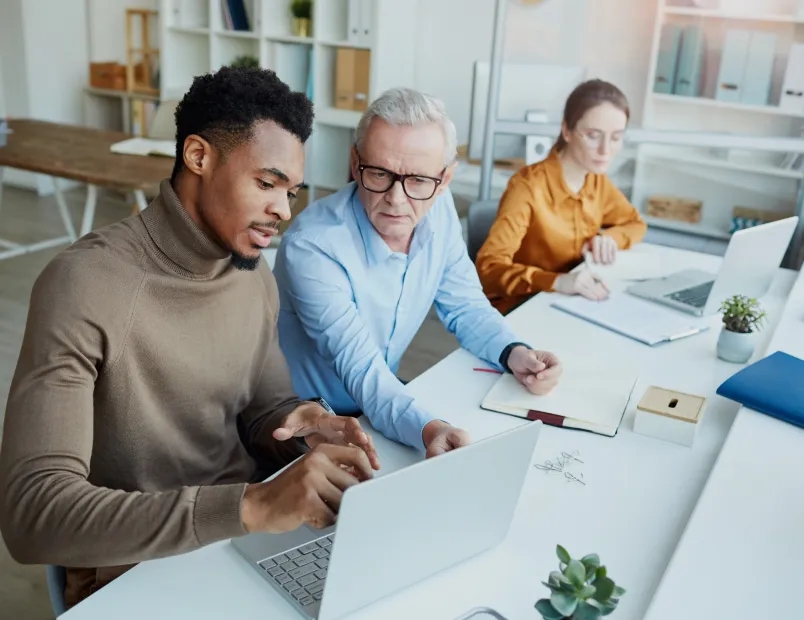 Three people sitting at a table, engrossed in their work on a laptop.