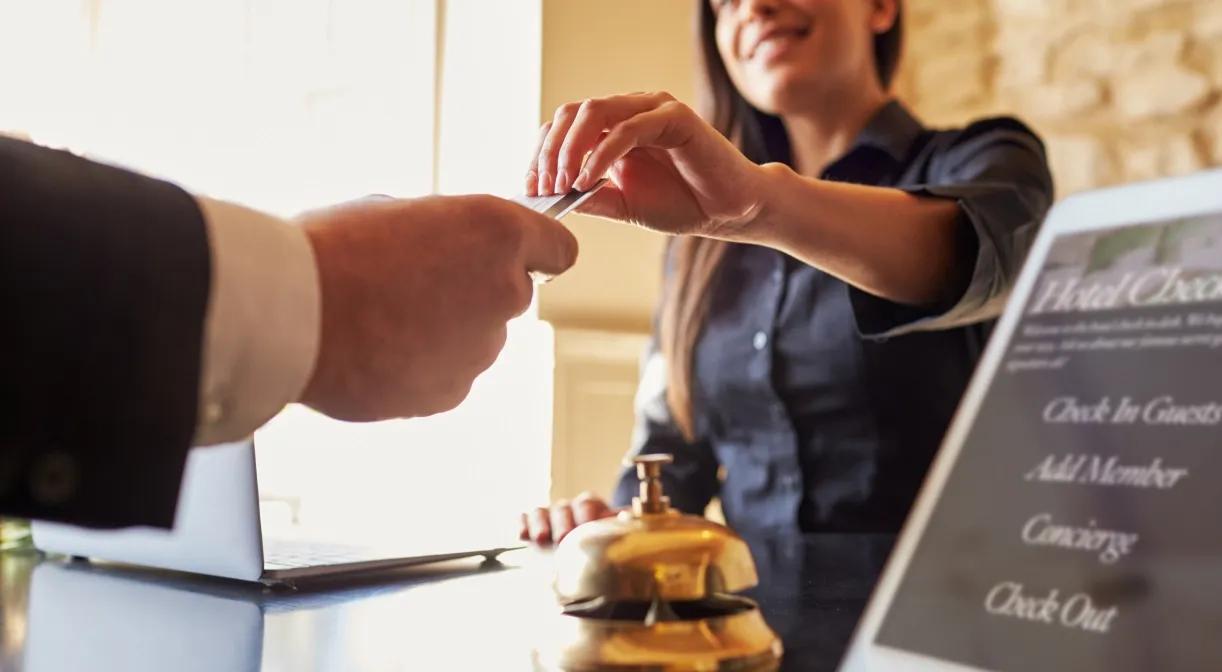 Woman handing man card at hotel desk.