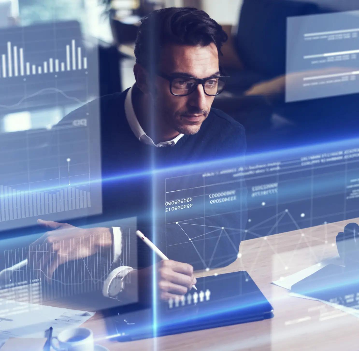 A man in glasses analyzing graphs on a screen.