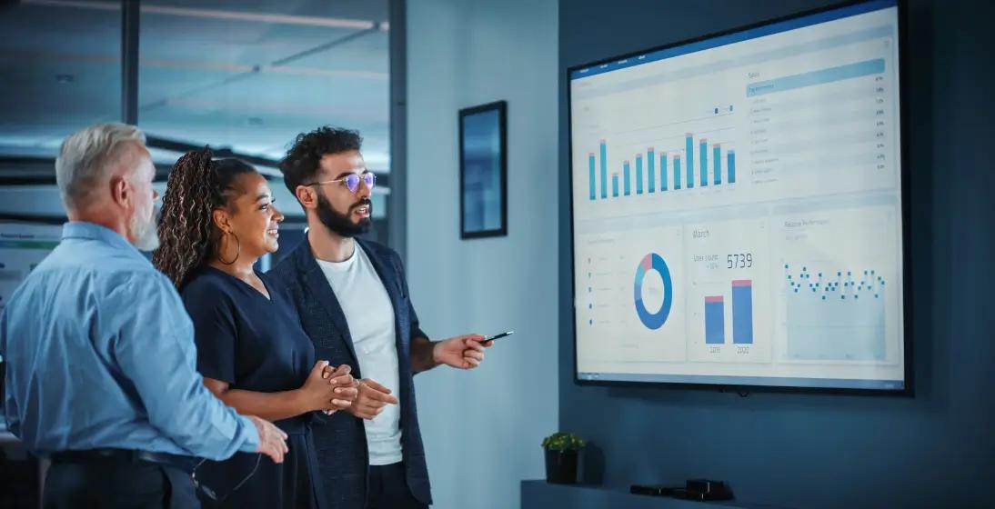 Three people standing before a large screen, engaged in outsourced data management discussion